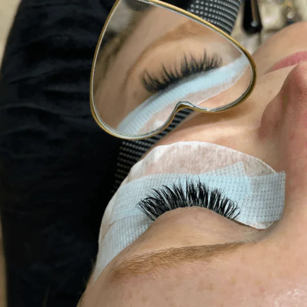 Lash extensions being applied, reflected in a heart-shaped mirror